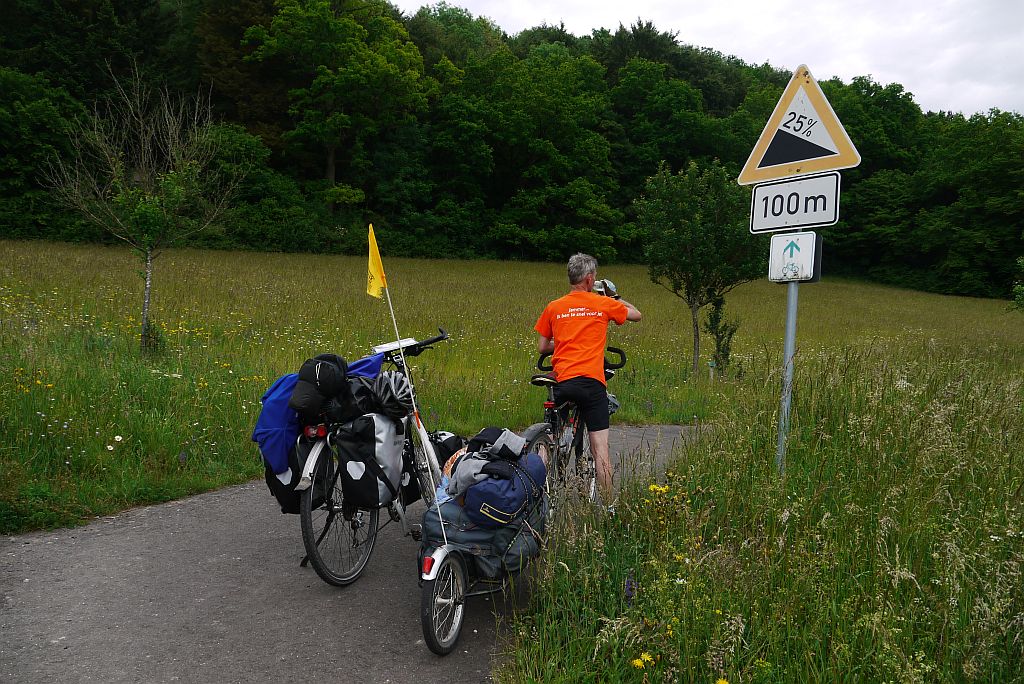 Michel en twee fietsen bij een verkeersbord waarop staat dat er een helling nadert van 25 procent