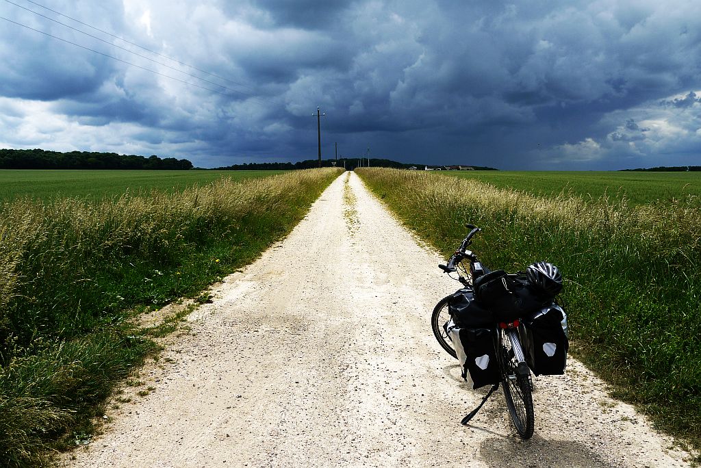 Foto van Raph's fiets op een onverharde weg met een dreigende wolkenlucht in de verte